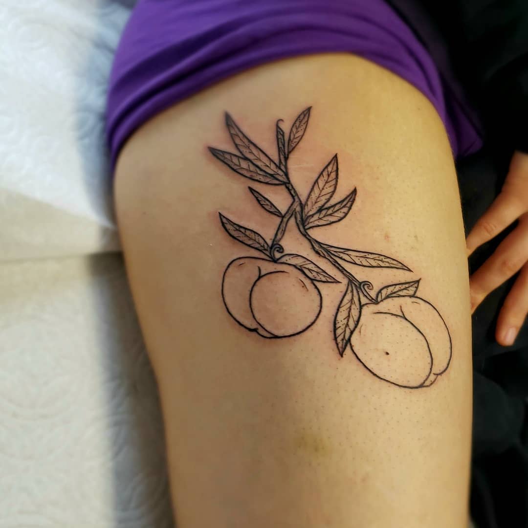 Tattoo of a branch with two peaches and leaves on an upper thigh